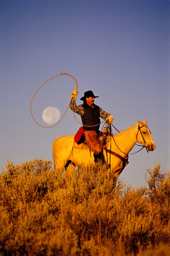 Cowboy sitting on horse with a full moon captured in his lasso; Seneca, Oregon, United States of America
