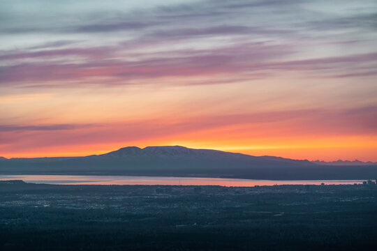 The sun sets above Mt. Susitna, or Sleeping Lady, across Cook Inlet from downtown Anchorage, Alaska on Dena&rsquo;ina land, with Knik arm in view; Alaska, United States of America