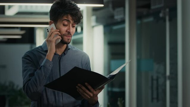 Businessman indian 30s man office lawyer entrepreneur talk mobile phone work with documentation check paper loan bills read documents discuss business contract speak distant wireless legal consultancy