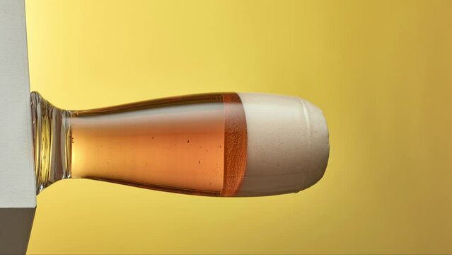 vertical format stop motion animation of beer pouring into glass on yellow background