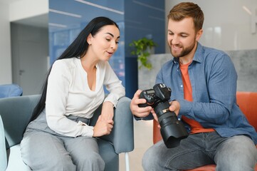 Photographer in office shows photo model in camera. Consultant adjusts activities company as whole. Photo session employees in workplace. Manager well-executed project. Photos best employees company.