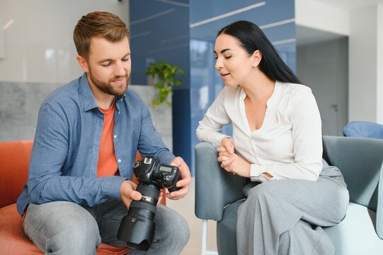 Photographer in office shows photo model in camera. Consultant adjusts activities company as whole. Photo session employees in workplace. Manager well-executed project. Photos best employees company.