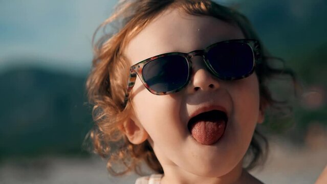 Cute little baby wearing sunglasses shows tongue close-up