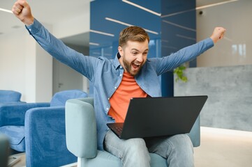 Photo of young excited man happy positive smile celebrate win victory success fists hands sit sofa home remote work.