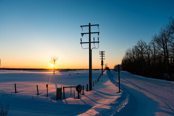 Snow-covered country road and farmland glowing pink with the setting sun; Alberta, Canada
