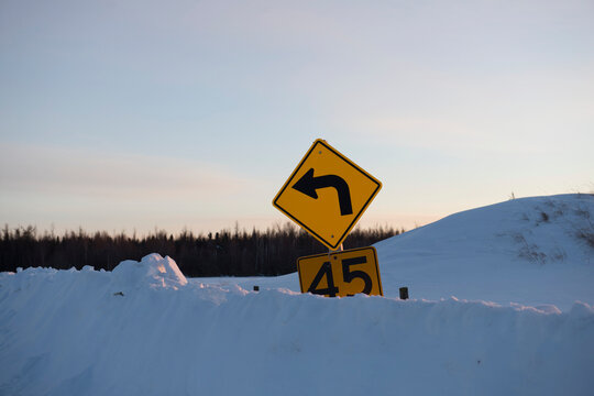 Yellow caution speed limit road sign buried in a deep snowbank; Alberta, Canada