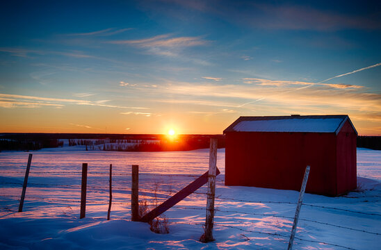 Sunset over the countryside in winter with a red shed in the foreground; Alberta, Canada