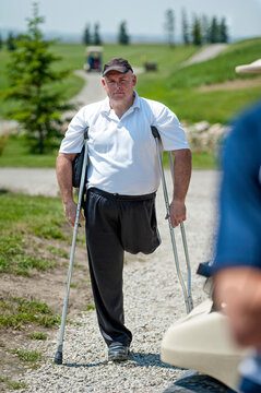 Man with amputated leg stands with crutches on a gravel path on a golf course, looking at the camera; Okotoks, Alberta, Canada