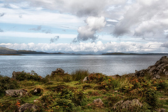 Autumn tinted ferns and ancient rocks show in the foreground to the sea and mountains beyond, dramatic cloudy sky, Sound of Jura; Argyll and Bute, Scotland