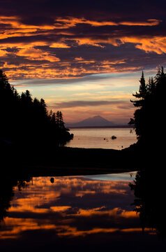 Sunset with reflections and clouds, looking west from Little Tutka Bay in Kachemak Bay, with Mount Redoubt in the background; Homer, Alaska, United States of America