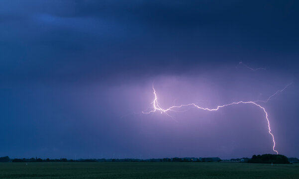 A lightning bolt arcs out of the base of a dark storm cloud and strikes the ground; Lincolnshire, England