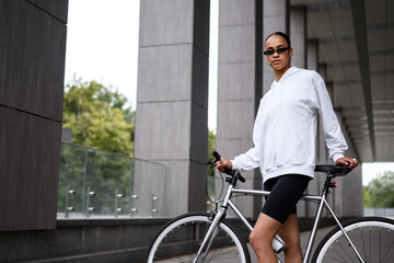 Young african american woman in stylish sunglasses standing near bike on street 