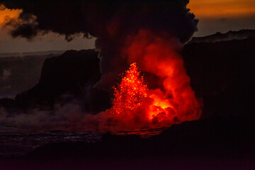 Red, hot lava spews on the ocean shoreline illuminating a huge column of noxious gas as it enters the water and lights up the darkness on the Big Island of Hawaii; Hawaii, United States of America
