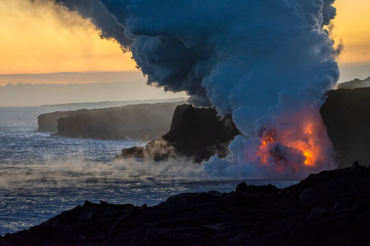 Hot lava illuminates a huge column of noxious gas as it enters the ocean on the Big Island of Hawaii; Hawaii, United States of America
