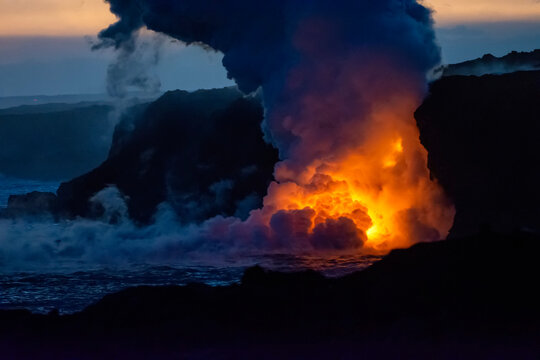 Hot lava illuminates a huge column of noxious gas as it enters the ocean and lights up the darkness on the Big Island of Hawaii; Hawaii, United States of America