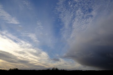 Amazing blue sky with clouds and sunshine. Line of horizon with forest at bottom of frame.
