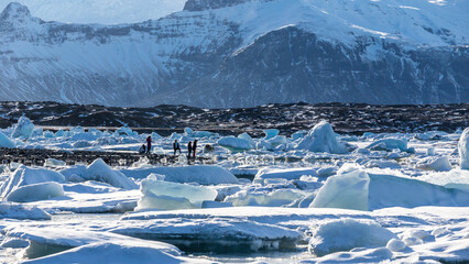 persone che camminano sul limitare della laguna del ghiacciaio Jökulsárlón, montagna innevata...