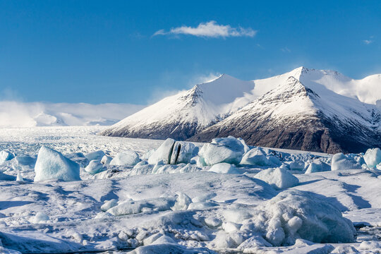 la laguna da scioglimento del ghiacciaio J&ouml;kuls&aacute;rl&oacute;n colma di iceberg con una montagna innevata, cielo azzurro e una nuvola