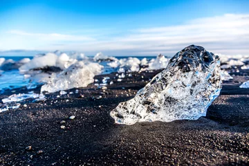 Fotobehang Blocco di ghiaccio su spiaggia nera e sabbiosa con mare sullo sfondo © frescofb