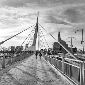 Pedestrians walk across the Esplanade Riel in The Forks District of Winnipeg with the Canadian Museum for Human Rights in the background; Winnipeg, Manitoba, Canada