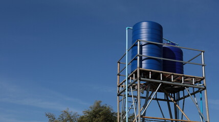Water reserve tank on the tower. Blue water tank on outdoor metal tower on bright blue sky background in bottom view and copy space with selective focus.