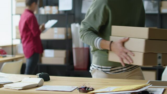 Cropped shot of courier picking up stack of parcel boxes from table in delivery service office