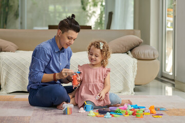 Smiling mother playing with daughter on floor in living room