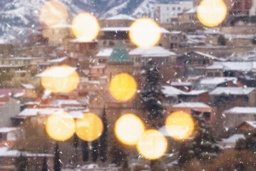 Beautiful winter blurred background of Tbilisi city with falling snow and bokeh lights