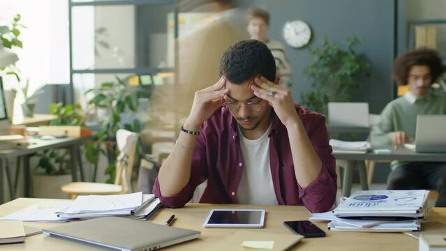 Timelapse of stressed overworked businessman sitting with head in hands while colleagues stacking papers on his desk in office