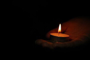 Woman holding burning candle in darkness, closeup. Space for text