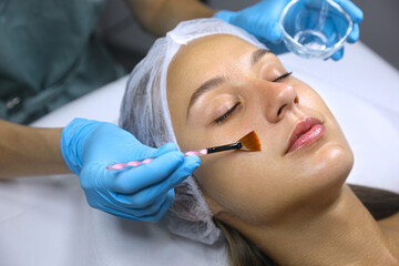 Cosmetologist applying chemical peel product on client's face in salon