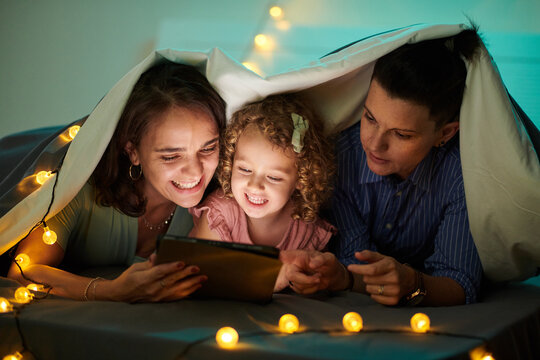 Happy family watching animated film on tablet computer when lying under blanket