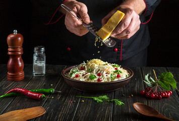 Professional chef adds cheese on spaghetti with vegetables in a plate. Menu or recipe for a delicious lunch for a hotel or restaurant