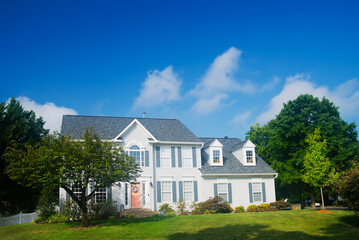 Single-family house in white color with a lawn and trees in front of the entrance. Blue sky on a summer day.