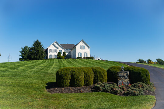 Large Modern White Stone House On A Hill With A Huge Green Lawn. Country Two-story House. Blue Sky On A Summer Day.