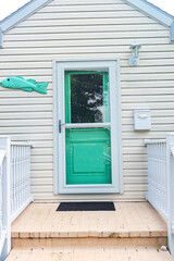 turquoise glazed front door of the house, decorated with fish. Facade of a porch house in a coastal town.