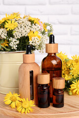 Bottles of essential oil and different wildflowers on wooden board