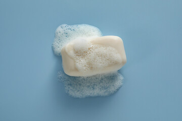 Soap bar with fluffy foam on light blue background, top view