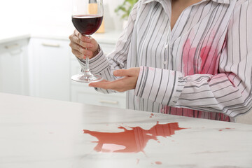 Woman with spilled wine over her shirt and marble table in kitchen, closeup - obrazy, fototapety, plakaty