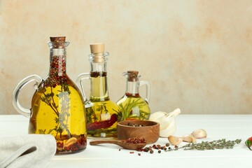 Cooking oil with different spices and herbs in jugs on white wooden table. Space for text