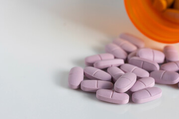 purple tablet pills with a spilt prescription medication bottle on a white background with copy space
