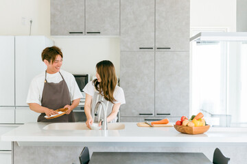 マイホームのキッチンで一緒に家事・お皿洗いををしながら会話する仲良しのアジア人夫婦の男女  © buritora