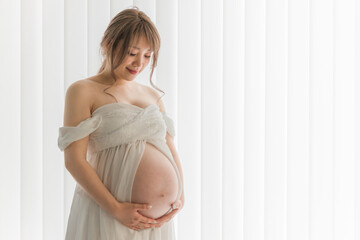 家のカーテンの前でマタニティフォトの撮影をする妊婦のアジア人女性
