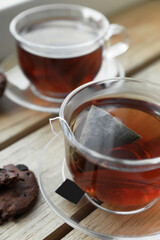 Bag of black tea in cups on wooden table indoors, closeup