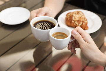 Man and woman drinking coffee at wooden table in outdoor cafe, closeup
