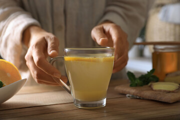 Woman making aromatic ginger tea at wooden table indoors, closeup