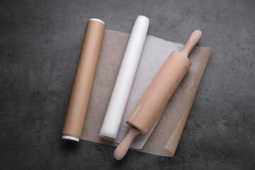 Rolls of baking paper and rolling pin on dark grey table, top view