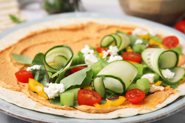 Tortilla with hummus and vegetables on table, closeup