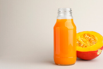 Tasty pumpkin juice in glass bottle and cut pumpkin on light background. Space for text