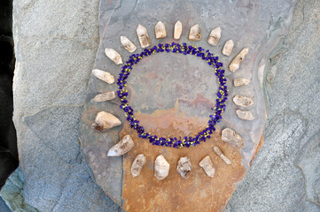 Raw quartz crystal and tiny purple flowers arranged in a circle meditation mandala on stone.. 
